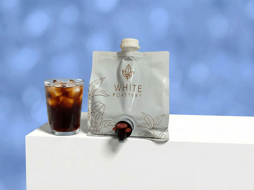 spouted pouch with tap dispenser next to a glass of iced coffee