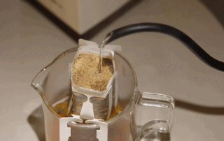 A drip coffee bag being brewed over a cup.