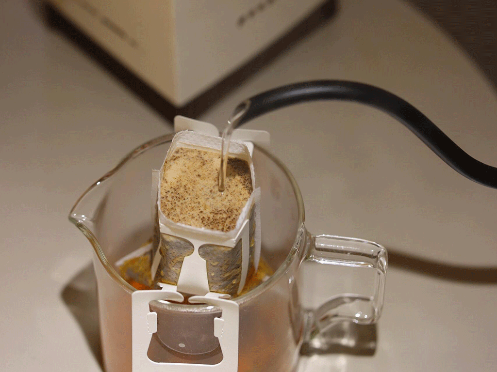 A drip coffee bag being brewed over a cup.