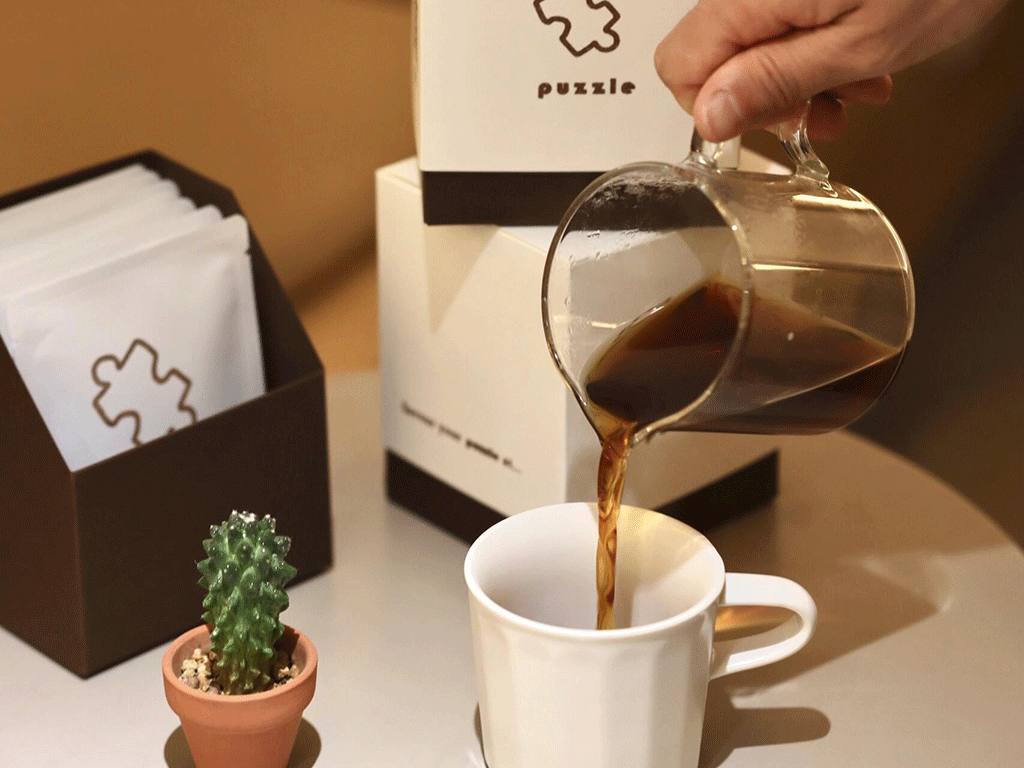 Pouring brewed coffee from a drip coffee bag into a cup with a cactus and drip coffee packaging boxes in the background.
