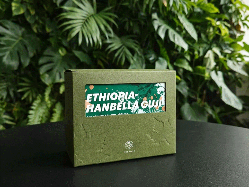 coffee-box-design-with-embossing-debossing-1 Debossing coffee box with recessed logo and subtle pattern details on a black table with green foliage in the background.