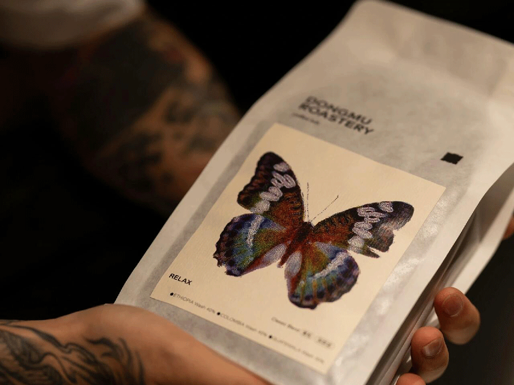 Hands holding a rice paper coffee bag with a butterfly label, showcasing sustainable packaging for coffee roasters