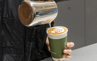 Barista pouring latte art into a takeaway coffee cup, illustrating the carbon footprint of a cup of coffee from farm to cup