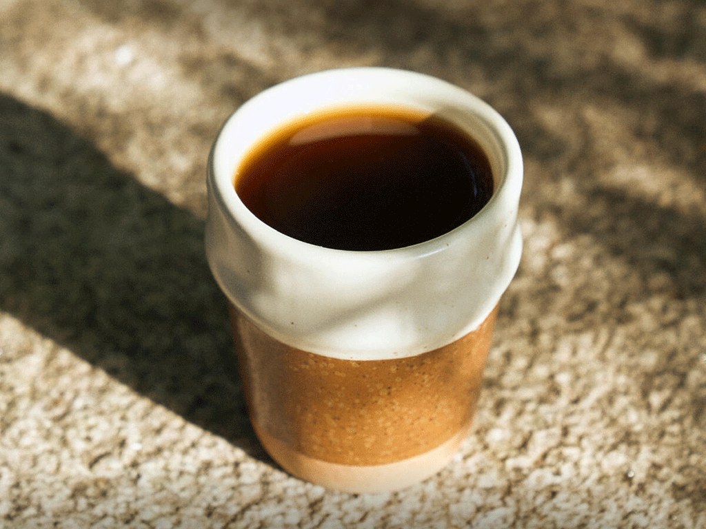 A cup of black Colombian coffee in a handmade ceramic cup placed on a stone surface in natural light