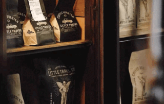Black and kraft flat bottom coffee bags with printed logos neatly arranged on wooden shelves, showcasing stylish packaging for small roasters.
