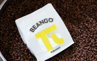Small white coffee bag displayed on roasted coffee beans to illustrate changing specialty coffee packaging sizes