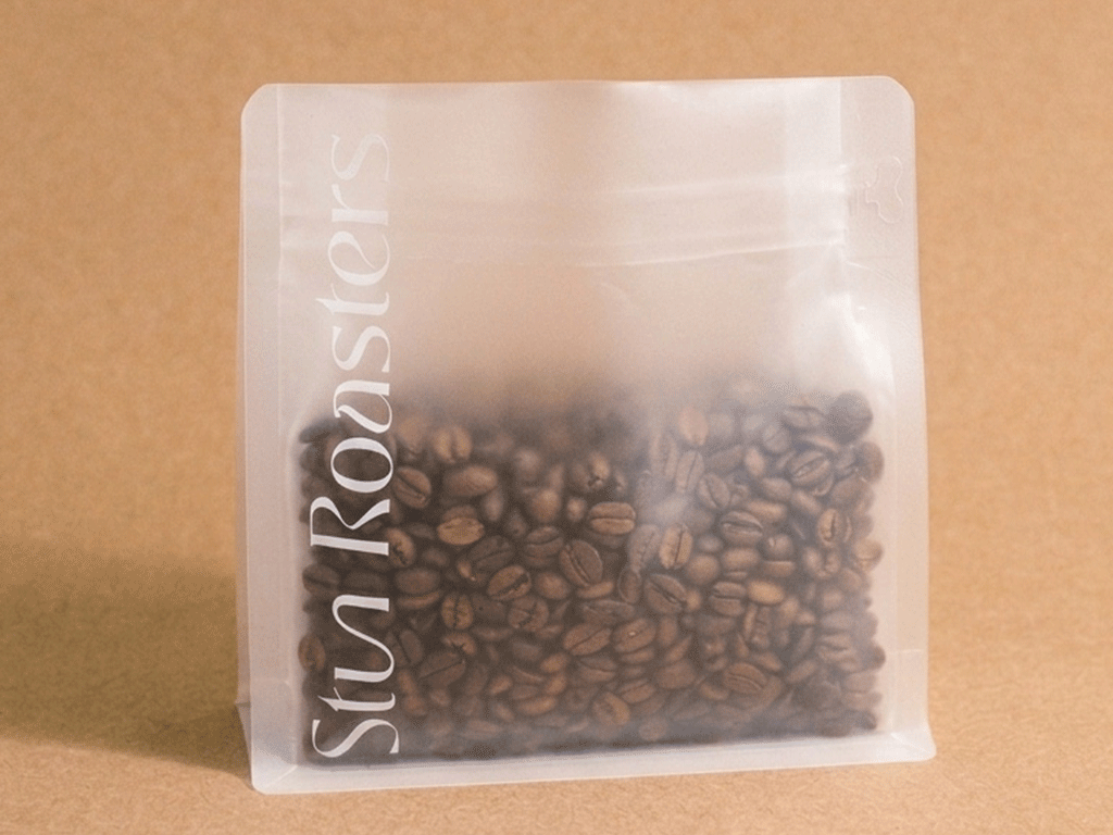 Frosted transparent coffee bag filled with roasted coffee beans on a kraft paper background