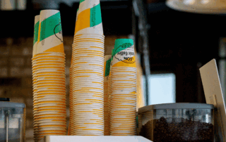 Stacks of paper hot coffee cups with custom branding and waterproof linings displayed on a counter.