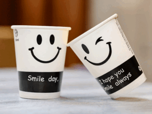 Two custom-designed paper coffee cups featuring playful smile graphics and sustainable packaging messages.