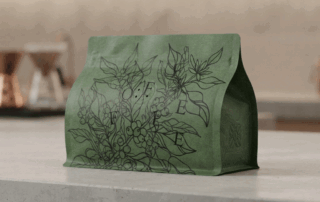A custom-designed green coffee bag with black botanical illustration, showcased in a professional setting.