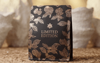 Black limited edition coffee bag with hot foil stamped leaf artwork on a natural textured background