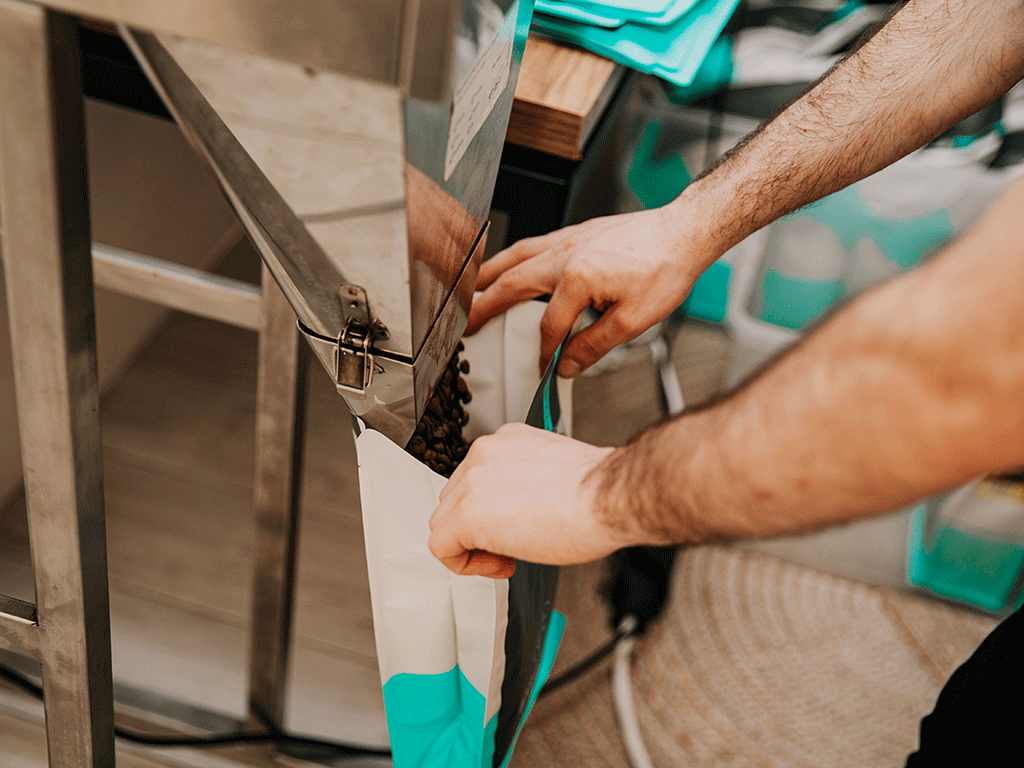 Coffee roaster filling freshly roasted coffee beans into a bag during the coffee packaging process