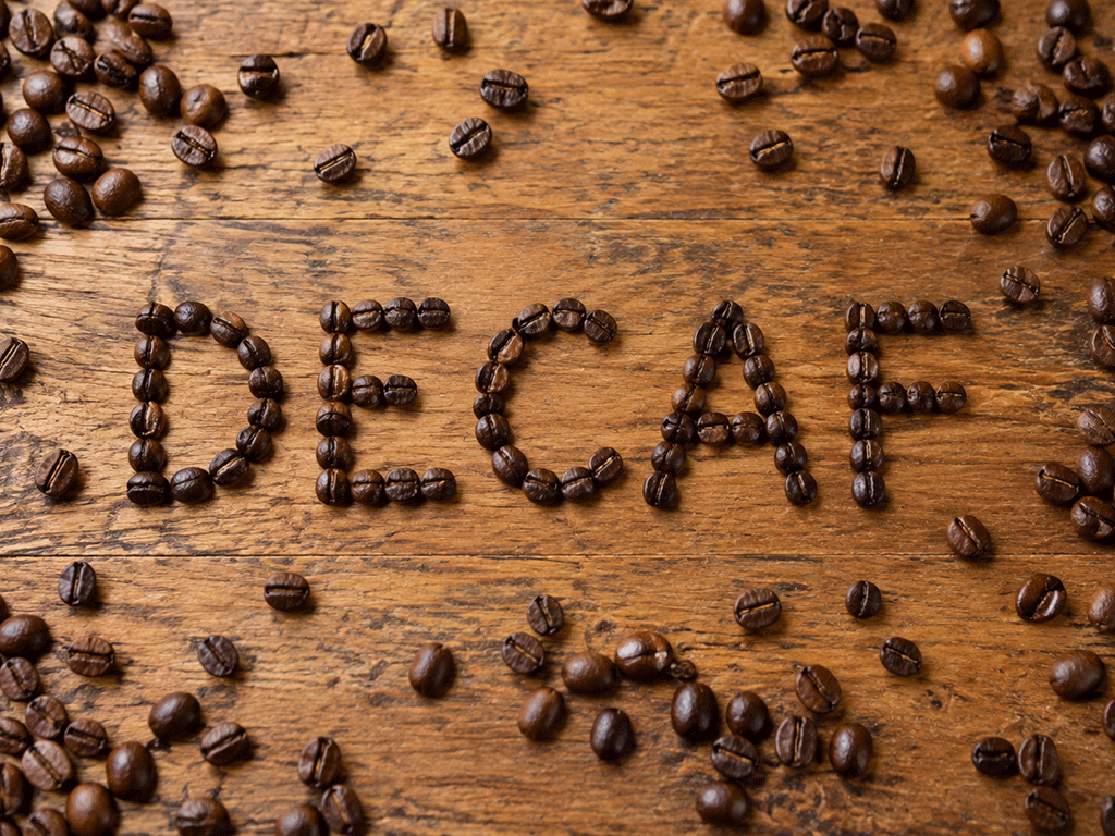 The word “DECAF” arranged with roasted coffee beans on a wooden surface